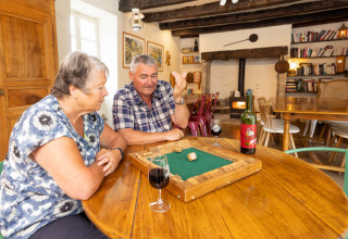 Coppia anziana gioca a un gioco da tavolo con vino a Le Moulin de Bel Air, campeggio in Occitania, Francia.