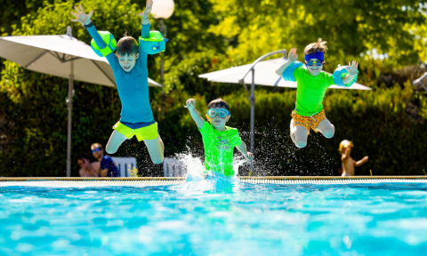 Tre bambini saltano nella piscina del campeggio Le Moulin de Bel Air, un villaggio vacanze in Occitania, Francia.