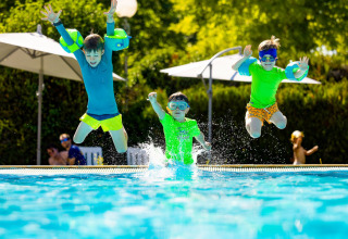 Tre bambini saltano nella piscina del campeggio Le Moulin de Bel Air, un villaggio vacanze in Occitania, Francia.