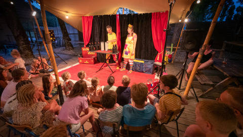 Children watch a magician performing on an outdoor stage at Le Moulin de Bel Air campsite, Occitanie, France.