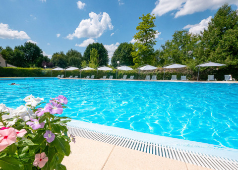 Outdoor pool at Campsite Le Moulin de Bel Air, Occitanie, France, with lounge chairs, umbrellas and flowers.