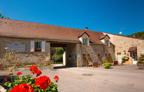 Foto del campeggio Le Moulin de Bel Air in Occitania, Francia, con edificio in pietra e fiori rossi.