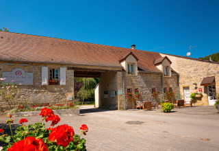 Foto del campeggio Le Moulin de Bel Air in Occitania, Francia, con edificio in pietra e fiori rossi.