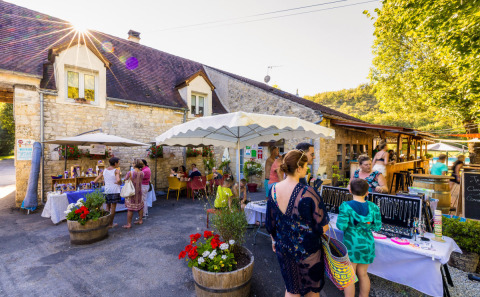 Visitatori tra le bancarelle al campeggio Le Moulin de Bel Air, Occitania, Francia, in una giornata soleggiata.