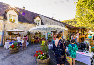 Visitatori tra le bancarelle al campeggio Le Moulin de Bel Air, Occitania, Francia, in una giornata soleggiata.