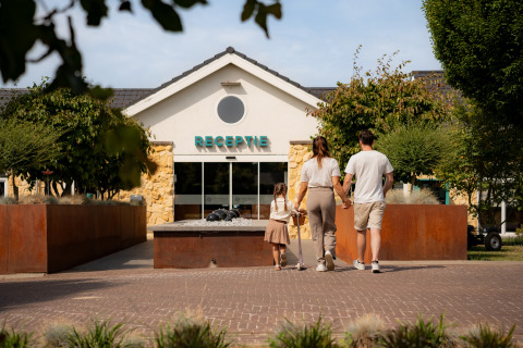 Una famiglia si dirige verso la reception di un lodge, circondata da alberi e una struttura accogliente.