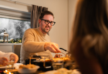 Man with glasses enjoying a cozy meal at a table in a lodge with snow falling outside the window.
