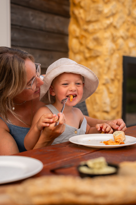 Une mère aide son enfant à manger à une table en bois à la Biesbosch Lodge, Resort Mooi Bemelen, Pays-Bas.