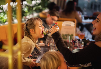 Een vrouw voert een vrolijk meisje in een sfeervolle lodge-restaurant met warme, gezellige inrichting.