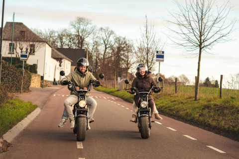 To personer kører el-scootere på en landevej nær lodge Biesbosch, Resort Mooi Bemelen, Holland.