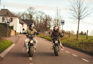 To personer kører el-scootere på en landevej nær lodge Biesbosch, Resort Mooi Bemelen, Holland.