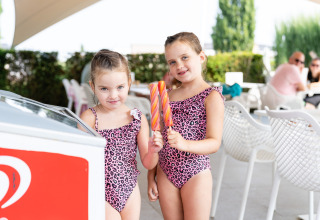 Twee meisjes met roze luipaardbadpakjes eten ijsjes buiten bij een lodge op een zonnige dag.
