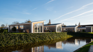 Lodge moderne au Resort Mooi Bemelen aux Pays-Bas, au bord d'un étang entouré de verdure sous ciel bleu.