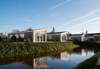 Lodge moderne au Resort Mooi Bemelen aux Pays-Bas, au bord d'un étang entouré de verdure sous ciel bleu.