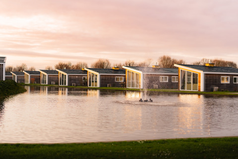 Moderne lodges aan het water met fontein bij Resort Mooi Bemelen, Biebosch, in Nederland bij zonsondergang.
