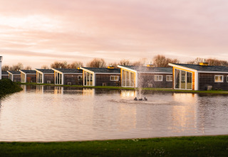 Moderne lodges aan het water met fontein bij Resort Mooi Bemelen, Biebosch, in Nederland bij zonsondergang.