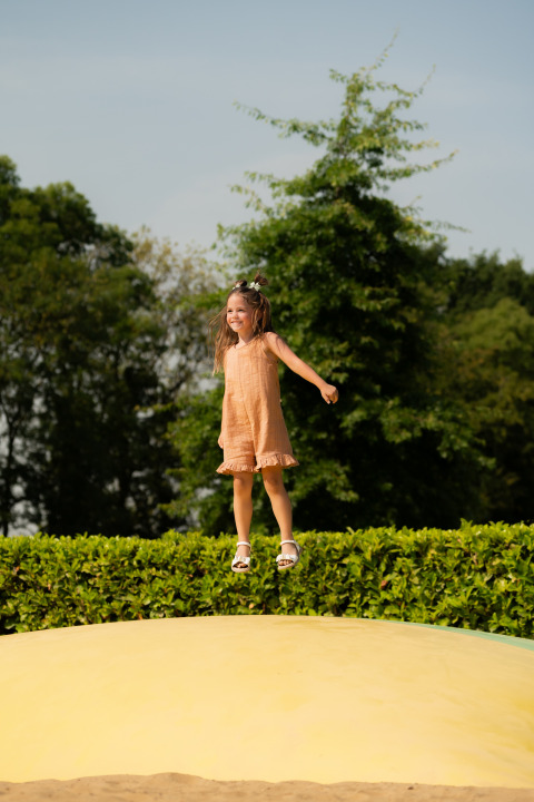 Een meisje springt lachend op een gele luchtkussen bij lodge Biebosch, Resort Mooi Bemelen, Nederland.