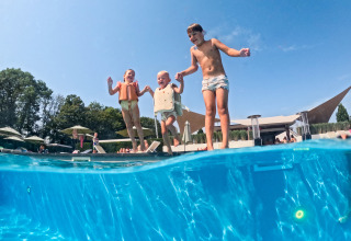 Kinderen met zwembandjes springen in het zwembad bij lodge Biebosch, Resort Mooi Bemelen in Nederland, op een zonnige dag.