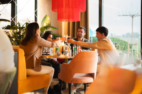 Quatre amis trinquent à une table au Lodge Biebosch du Resort Mooi Bemelen aux Pays-Bas dans une ambiance conviviale.