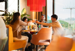 Vier vrienden proosten aan een tafel bij Lodge Biebosch in Resort Mooi Bemelen, Nederland, gezellige sfeer.