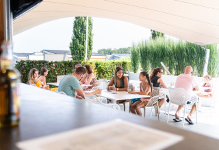 Mensen ontspannen en kletsen op het terras van een lodge onder een grote zonneluifel in de zomer.