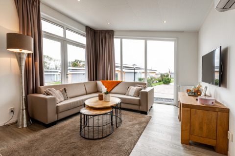 Moderne lodge woonkamer met grote ramen, beige bank, houten tafels, vloerkleed en een muur-tv.