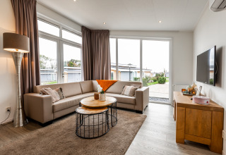 Moderne lodge woonkamer met grote ramen, beige bank, houten tafels, vloerkleed en een muur-tv.
