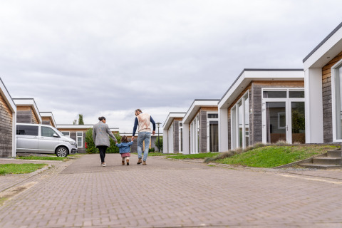 Gezin wandelt tussen moderne lodges bij Resort Mooi Bemelen, lodge Biebosch, op een bewolkte dag.