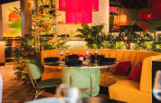 Stylish restaurant lounge with a yellow sofa, green chairs, Christmas tree and lush green plants.