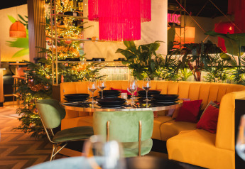 Farverig restaurantindretning med gul sofa, grønne stole, pyntede juletræer og levende planter.