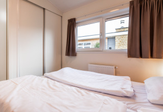 Chambre dans une lodge avec lit double, draps blancs, grandes fenêtres et rideaux marron.