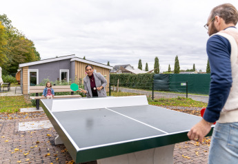 Gezin speelt een potje tafeltennis buiten bij een lodge van Resort Mooi Bemelen in Nederland.