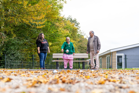 Drie mensen spelen jeu de boules op een bladrijke baan bij lodge Biebosch, Resort Mooi Bemelen, Nederland.