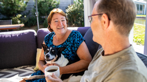 Un couple souriant et leur chien se détendent sur la terrasse du lodge Biebosch, Resort Mooi Bemelen, Pays-Bas.