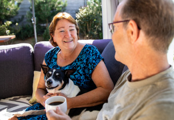 Un couple souriant et leur chien se détendent sur la terrasse du lodge Biebosch, Resort Mooi Bemelen, Pays-Bas.