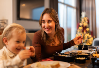 Une mère et son enfant partagent un repas chaleureux à table, avec un sapin de Noël illuminé derrière.