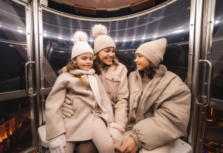 Trois personnes en manteaux d'hiver et bonnets sourient ensemble dans une gondole à Resort Mooi Bemelen, Pays-Bas.