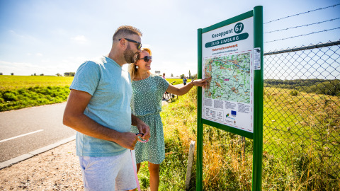 Dos personas observan un mapa de rutas ciclistas en un cartel bajo el sol de Zuid-Limburg.