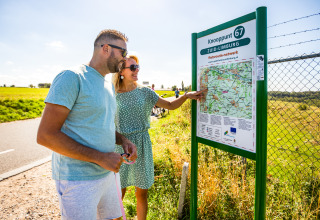 Twee personen bekijken een fietsroutekaart aan een knooppuntbord in het zonnige Zuid-Limburg.