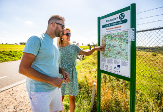 Deux personnes consultent une carte cyclable sur un panneau, sous le soleil de Zuid-Limburg.