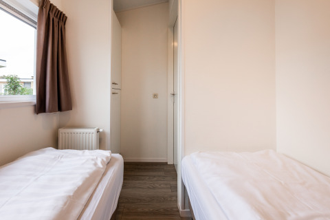 Helles Zimmer in einer Lodge mit zwei Einzelbetten, weißer Bettwäsche, Holzboden und Fenster mit Vorhang.