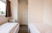 Helles Zimmer in einer Lodge mit zwei Einzelbetten, weißer Bettwäsche, Holzboden und Fenster mit Vorhang.