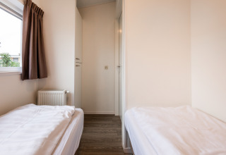 Helles Zimmer in einer Lodge mit zwei Einzelbetten, weißer Bettwäsche, Holzboden und Fenster mit Vorhang.