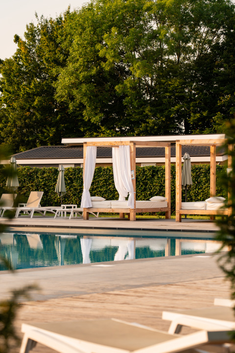 Espace piscine extérieure dans un lodge avec transats, baldaquins blancs et arbres verdoyants en arrière-plan.