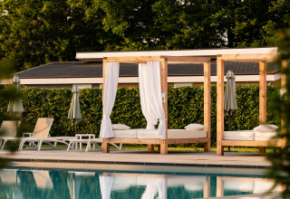 Espace piscine extérieure dans un lodge avec transats, baldaquins blancs et arbres verdoyants en arrière-plan.