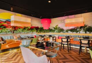 Intérieur de restaurant tendance avec sièges colorés, plantes et néon chez Biebosch - Sunshower, Resort Mooi Bemelen.