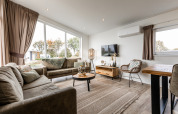 Salon moderne au lodge Biebosch - tuinhuis avec grandes fenêtres, canapés confortables et sol en bois.