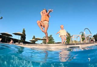 Deux enfants avec gilets de sauvetage jouent et sautent près de la piscine à Biebosch - tuinhuis, Resort Mooi Bemelen.