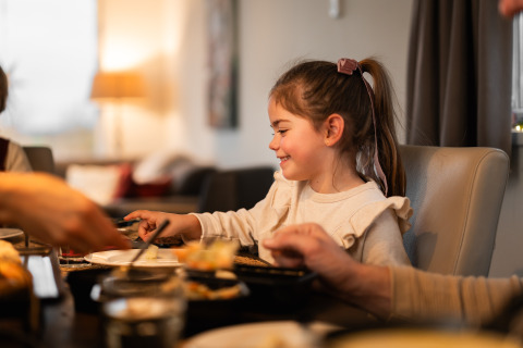 Une jeune fille sourit en mangeant à la table de Biebosch - tuinhuis, Resort Mooi Bemelen, Pays-Bas.