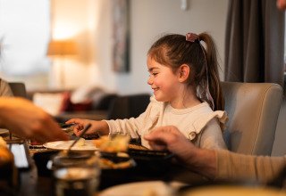 Une jeune fille sourit en mangeant à la table de Biebosch - tuinhuis, Resort Mooi Bemelen, Pays-Bas.
